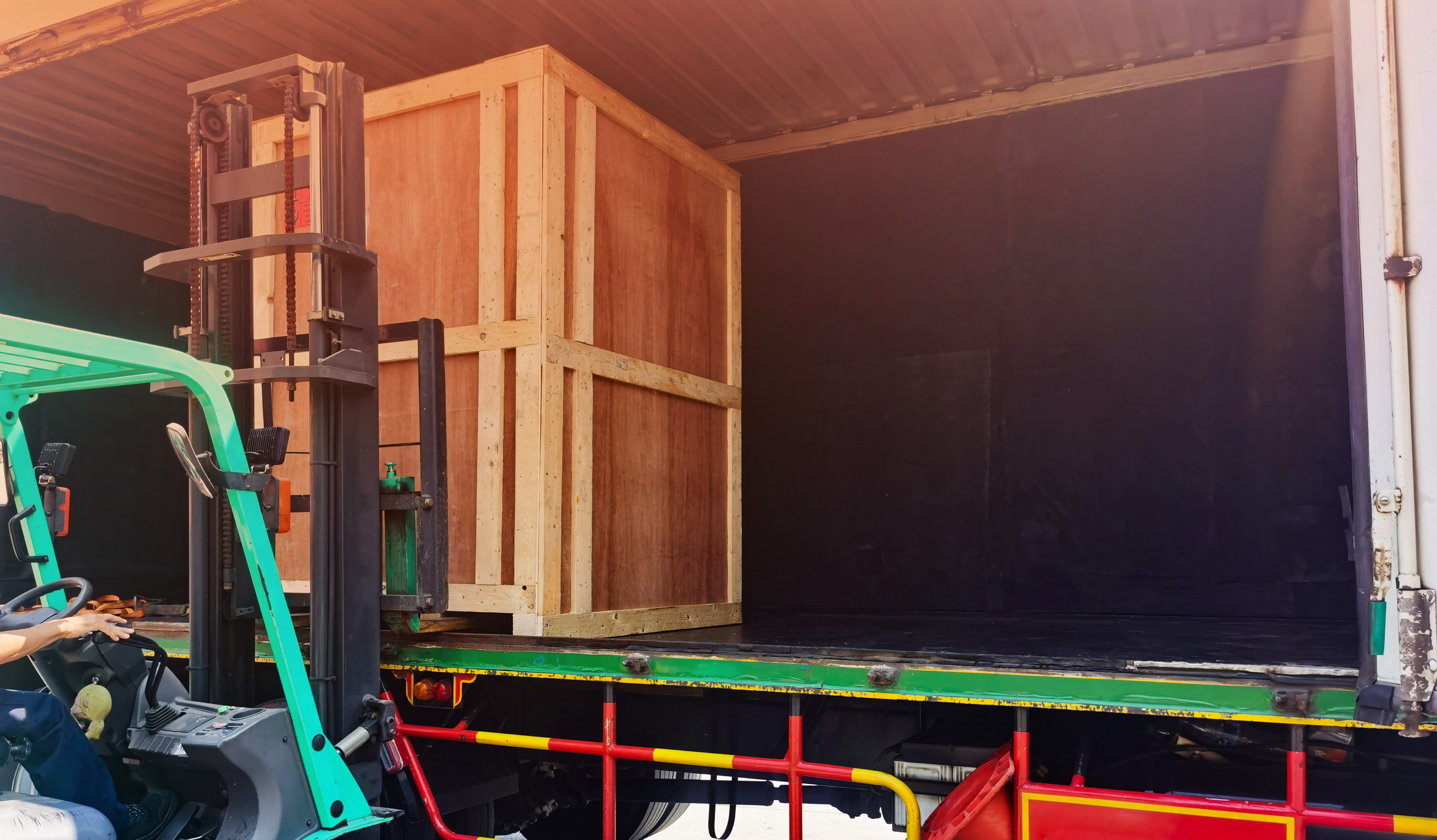 Worker driving forklift loading shipment carton boxes goods on wooden pallet at loading dock from container truck to warehouse cargo storage in freight logistics, transportation industrial, delivery